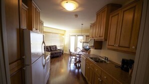 A compact kitchen with wooden cabinets, a refrigerator, a dining area with a table and chairs, and a television.