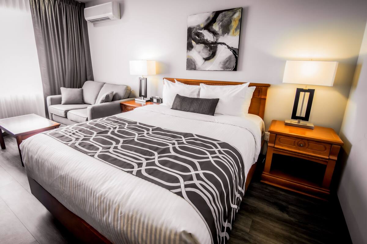 A hotel room with a large bed, a bedside table, a nightstand, a chair, a desk, and a wall-mounted air conditioner.