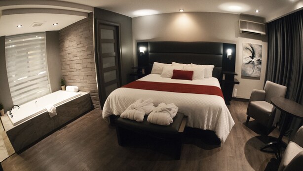 A modern hotel room with a large bed, a separate seating area, a bathtub, and a flat-screen TV.