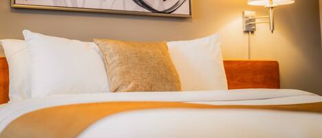 Una cama bien hecha con ropa de cama blanca y beige, un cuadro abstracto grande en la pared y una lámpara de noche.