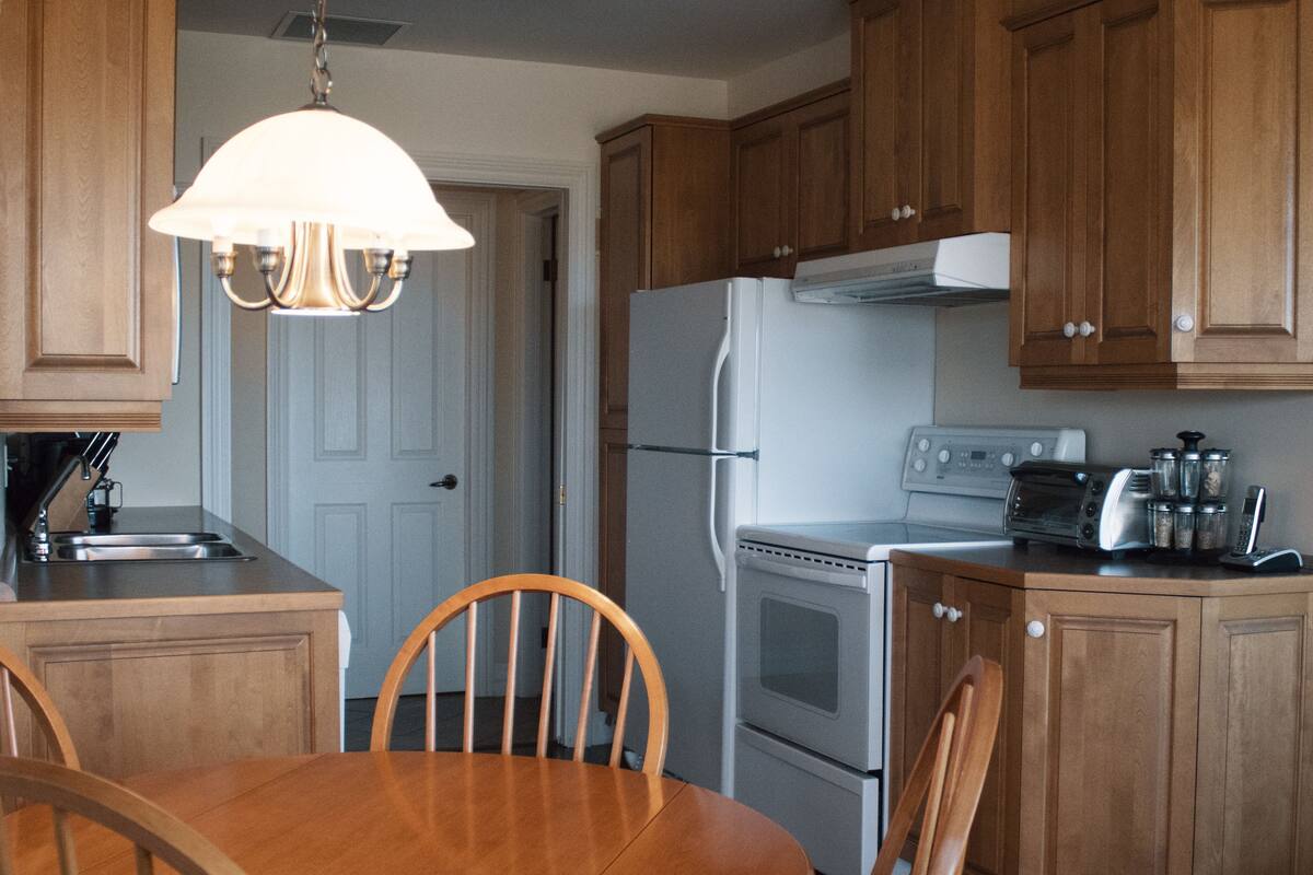 A kitchen with wooden cabinets, a stove, a refrigerator, a sink, and a dining table with chairs.
