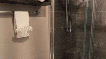 A bathroom with a toilet, a glass-enclosed shower, and a shelf with rolled towels.