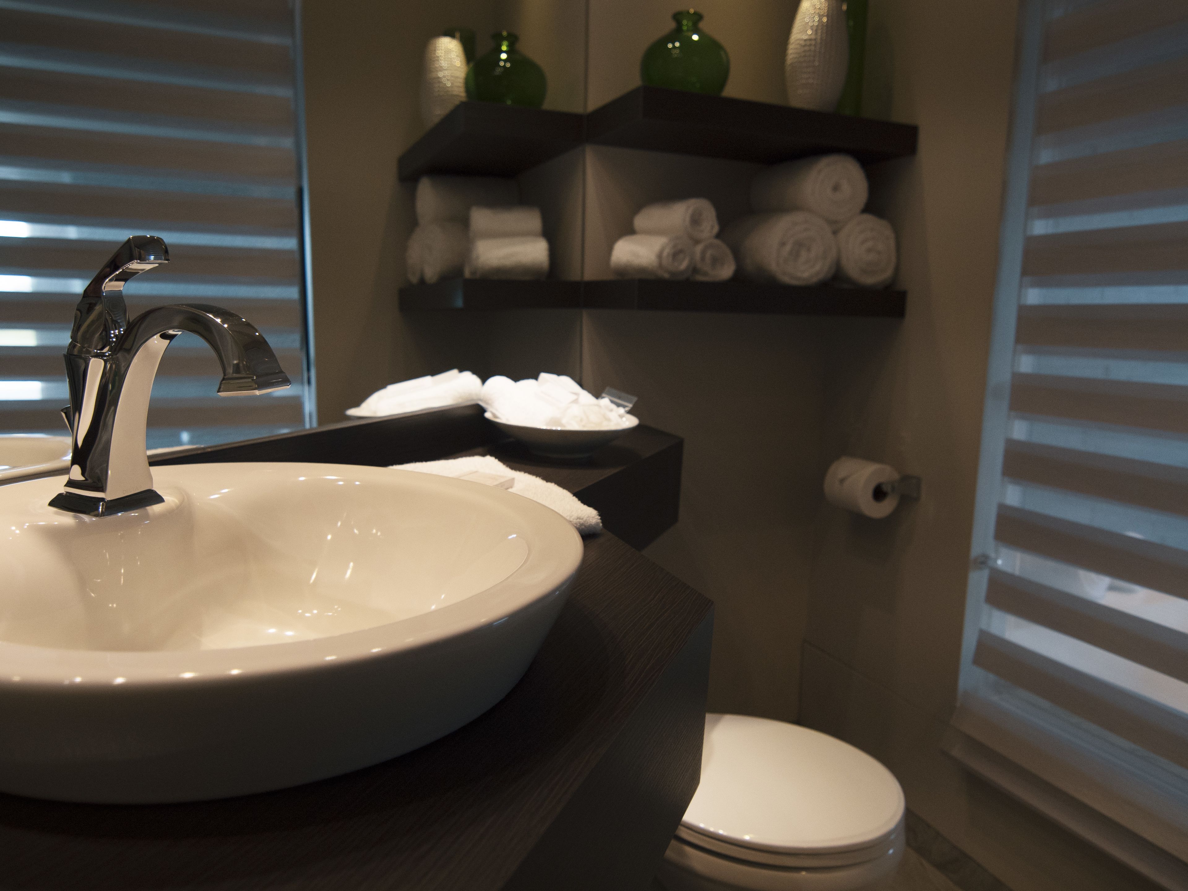 A bathroom with a round sink, a toilet, and a shelf with towels and toiletries.