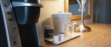Une machine à café Keurig posée sur une table en bois, avec une lampe et une cafetière en arrière-plan.
