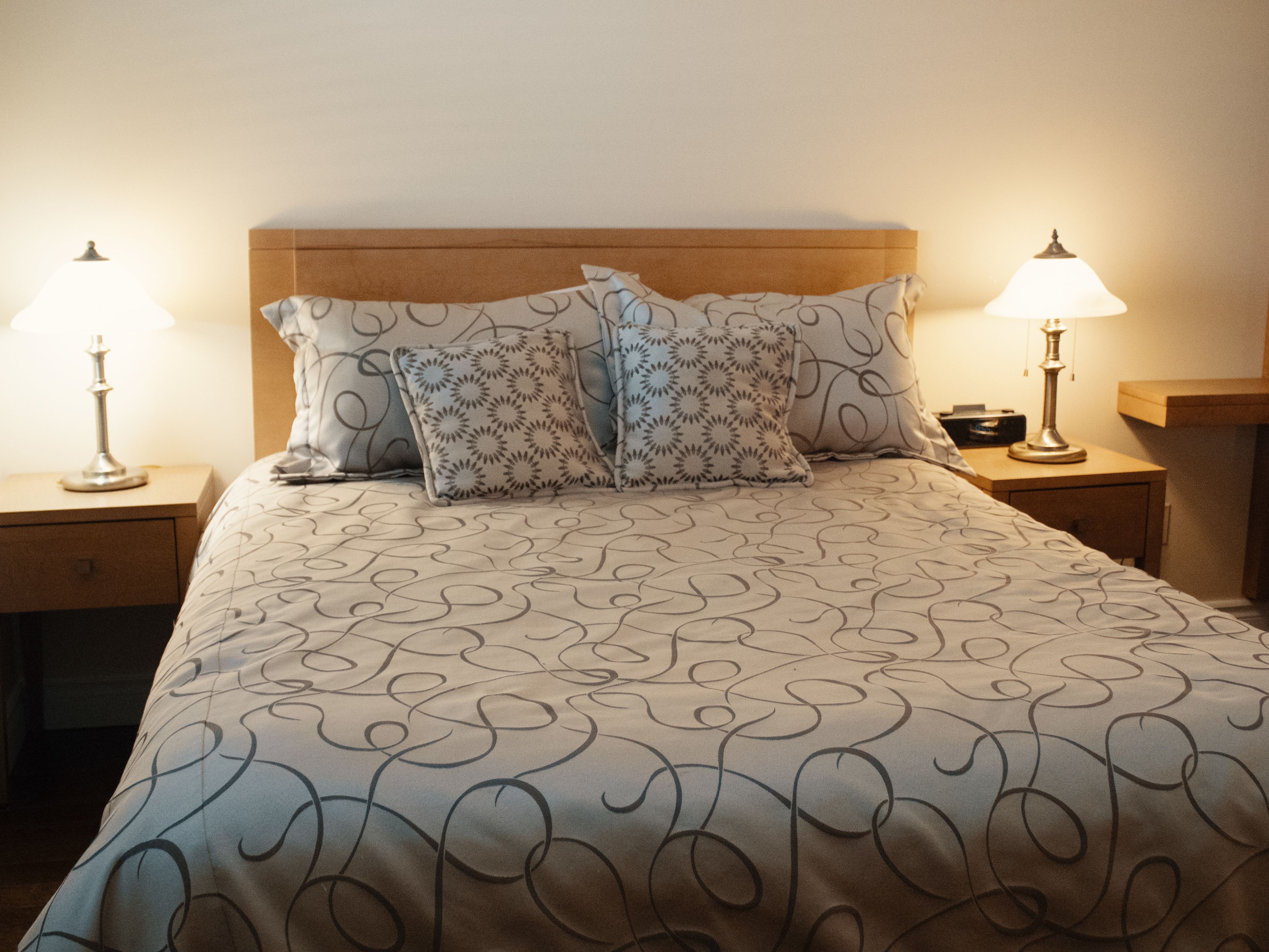 A neatly made bed with a patterned bedspread, two decorative pillows, and two bedside lamps on wooden nightstands.