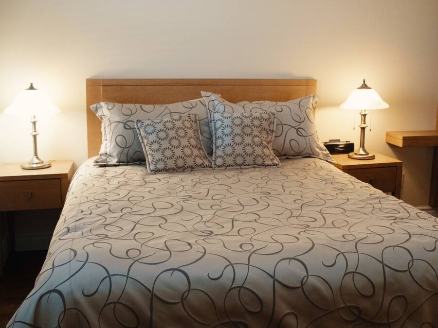 A neatly made bed with a patterned bedspread, two decorative pillows, and two bedside lamps on wooden nightstands.