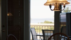 A dining area with a table and chairs, a lamp, and a view of the ocean through a door.