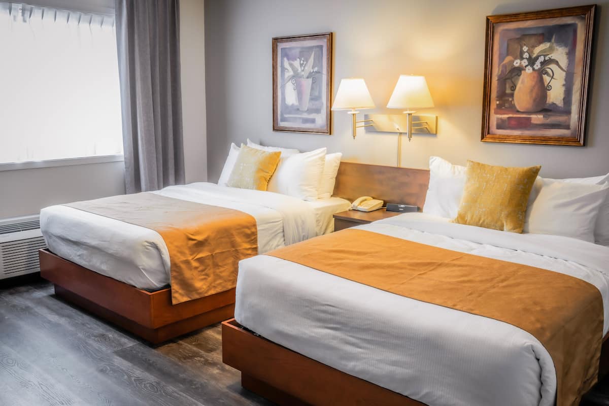 A hotel room with two beds, a bedside table with a lamp, a phone, and framed artwork on the wall.