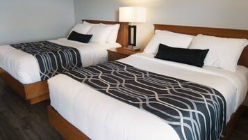 Two double beds with patterned bedspreads, a bedside table with a lamp, and a wooden floor.