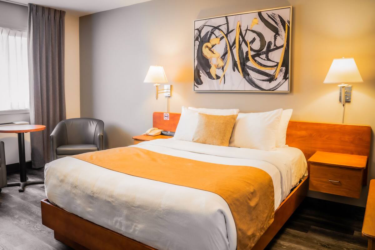 A hotel room with a large bed, a desk, a chair, and a painting on the wall.