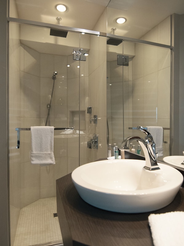 A modern bathroom with a glass-enclosed shower, a white sink, and a mirror. - Hôtel le Voyageur (Sept-Iles)