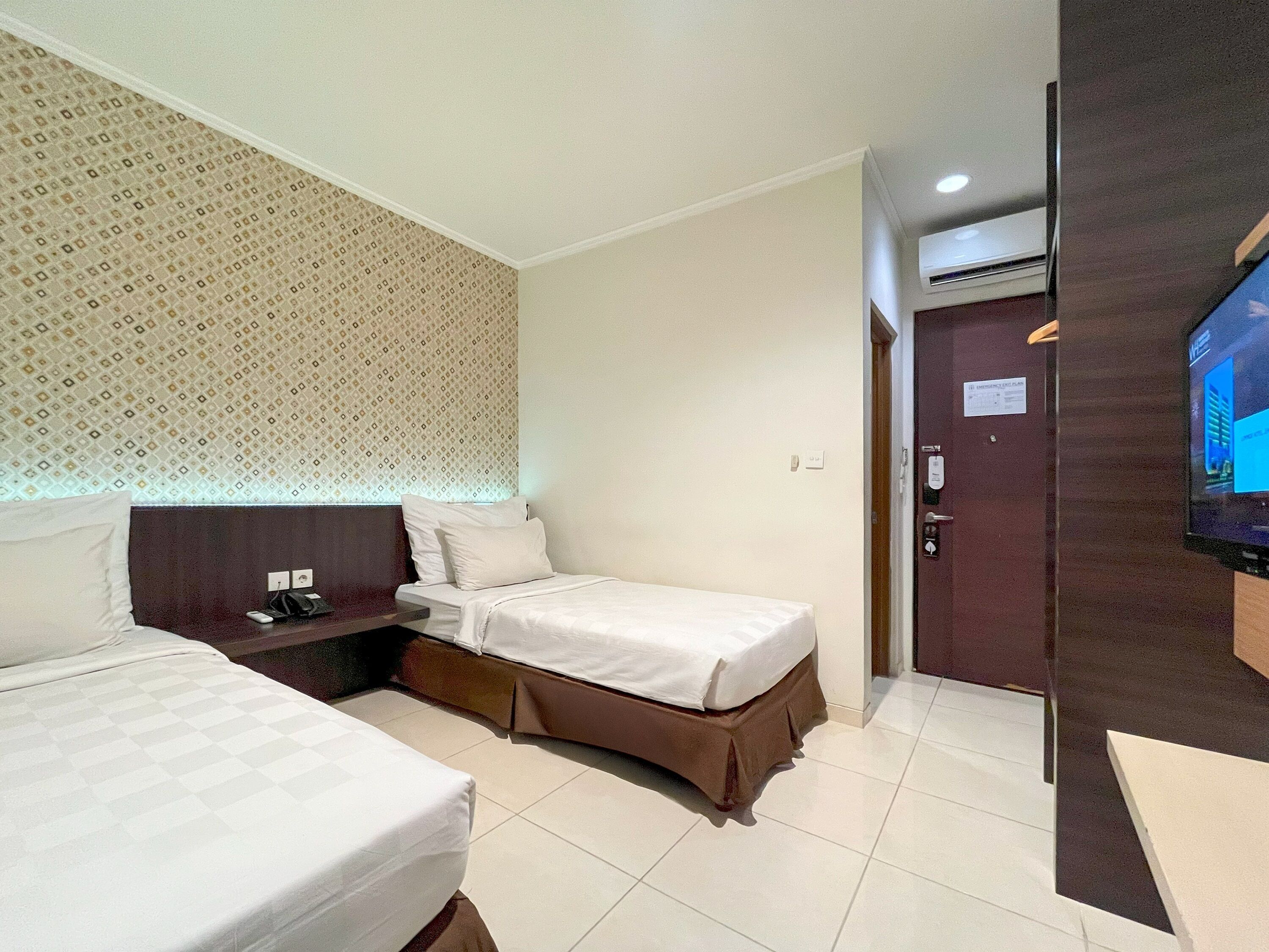A hotel room with two beds, a small desk, a TV, and a door with a sign.