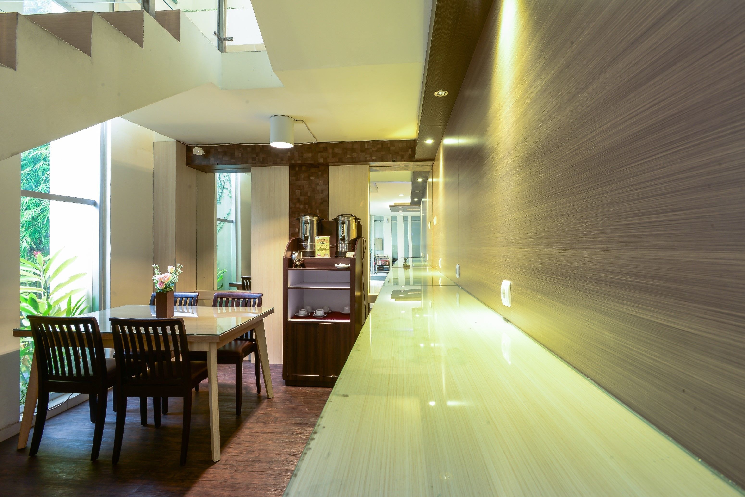 A modern kitchen with a long counter, wooden chairs, and a built-in shelf with kitchenware.