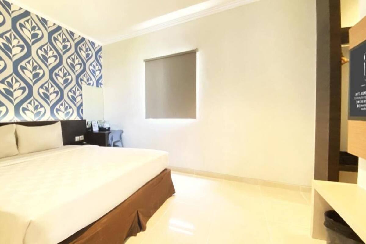 Una habitación de hotel con una cama grande, un papel tapiz decorativo, un ventanal pequeño y un escritorio con una silla.