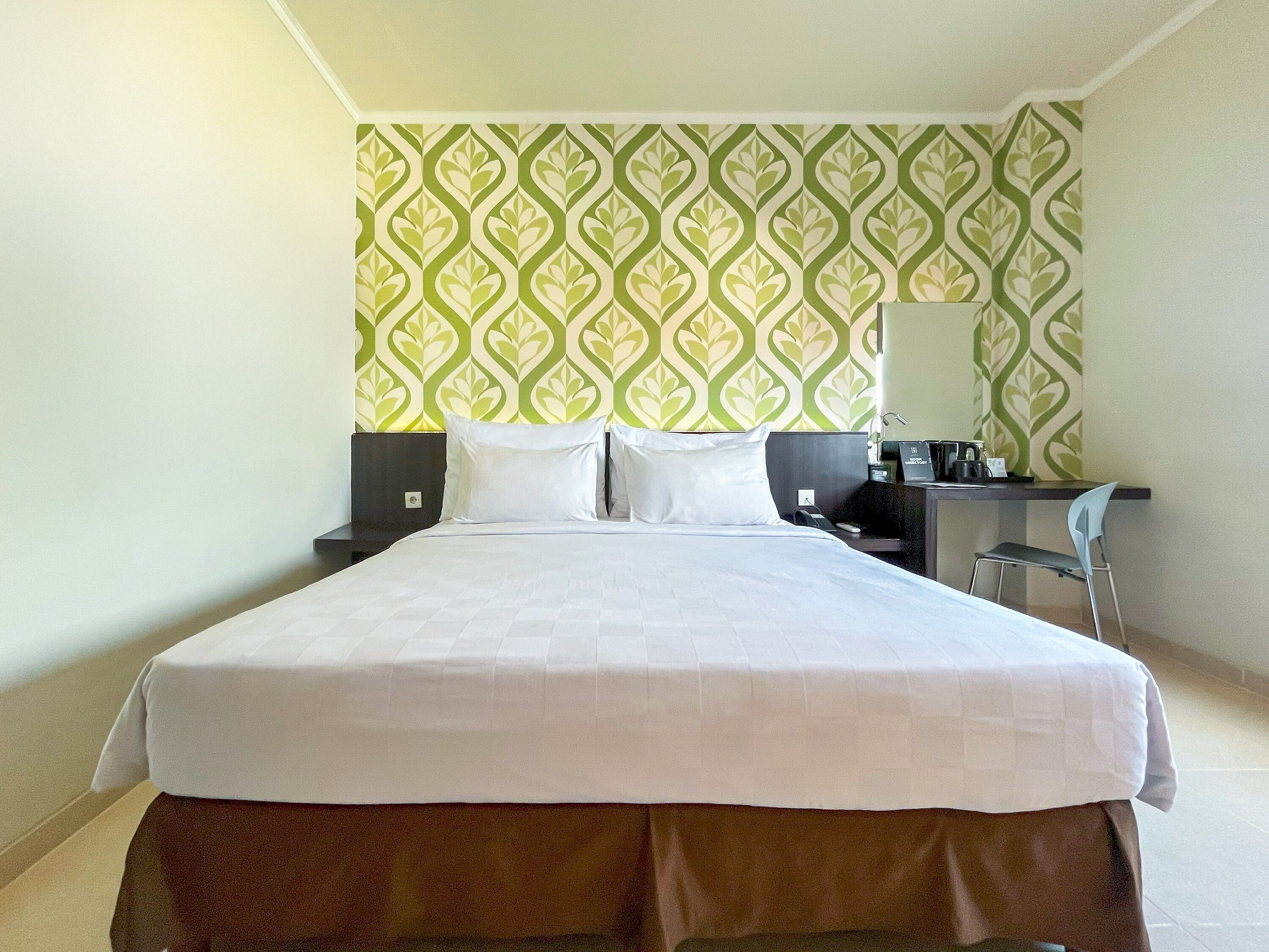 A hotel room with a large bed, a desk with a chair, a coffee machine, and a wall with a green and white pattern.