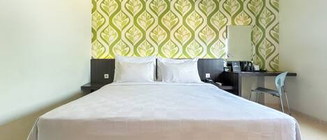 A hotel room with a large bed, a desk with a chair, a coffee machine, and a wall with a green and white pattern.