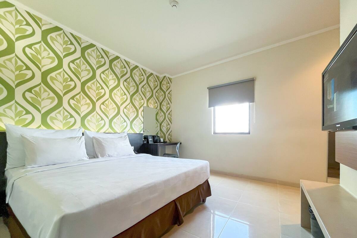 Habitación de hotel con una cama grande, un escritorio pequeño, televisión y ventana con vistas.