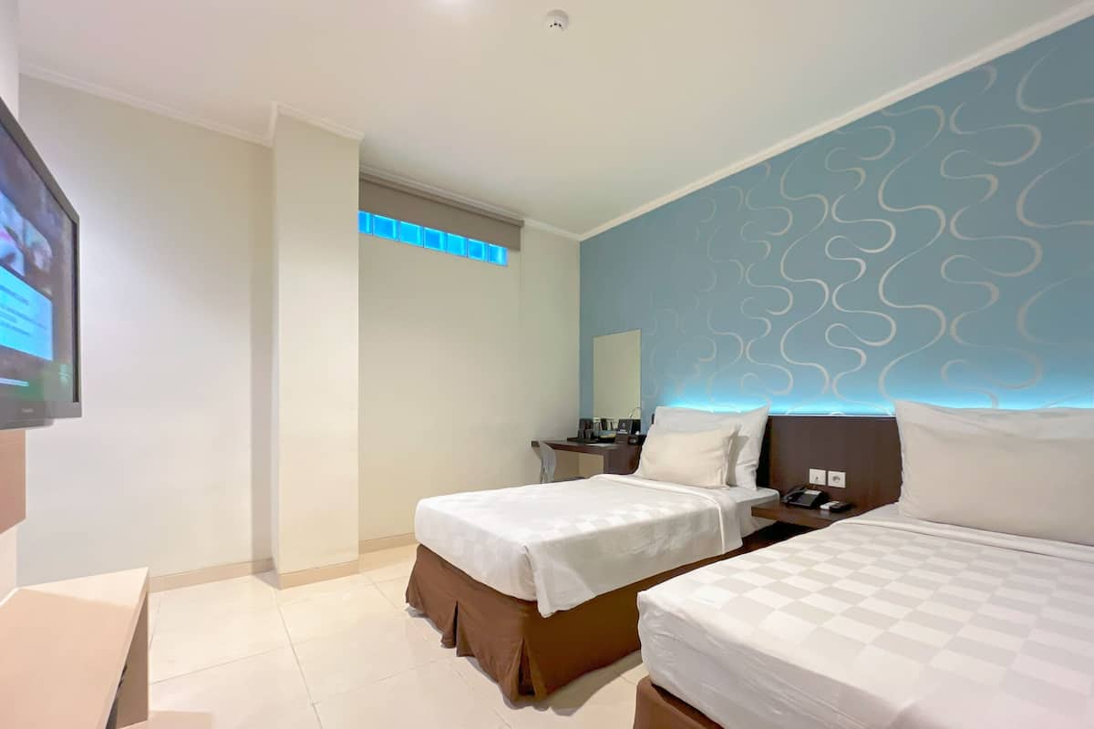 Habitación de hotel con dos camas, televisión, escritorio y baño con ducha.