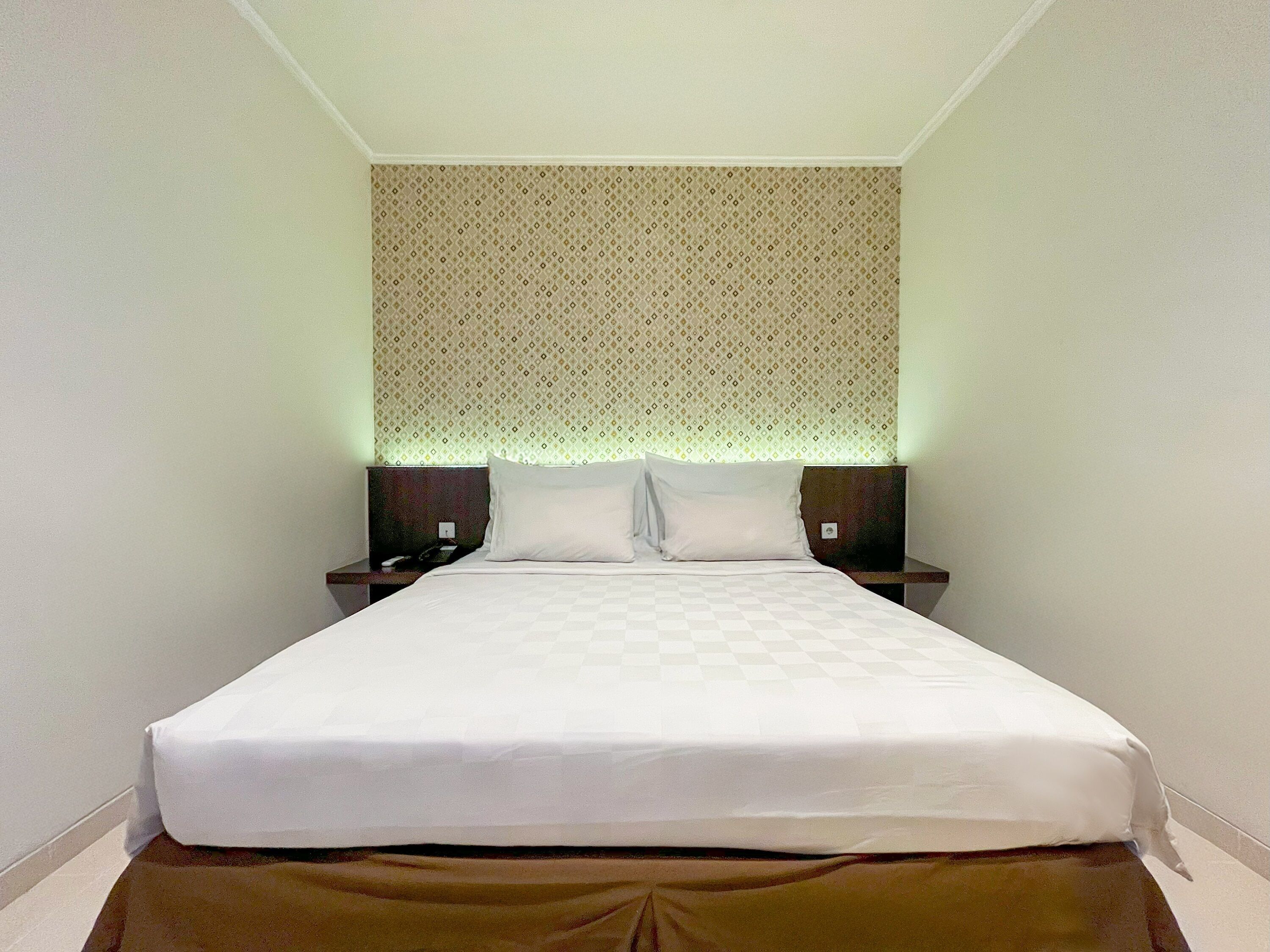 A neatly made bed with white linens, two bedside tables, and a patterned headboard.