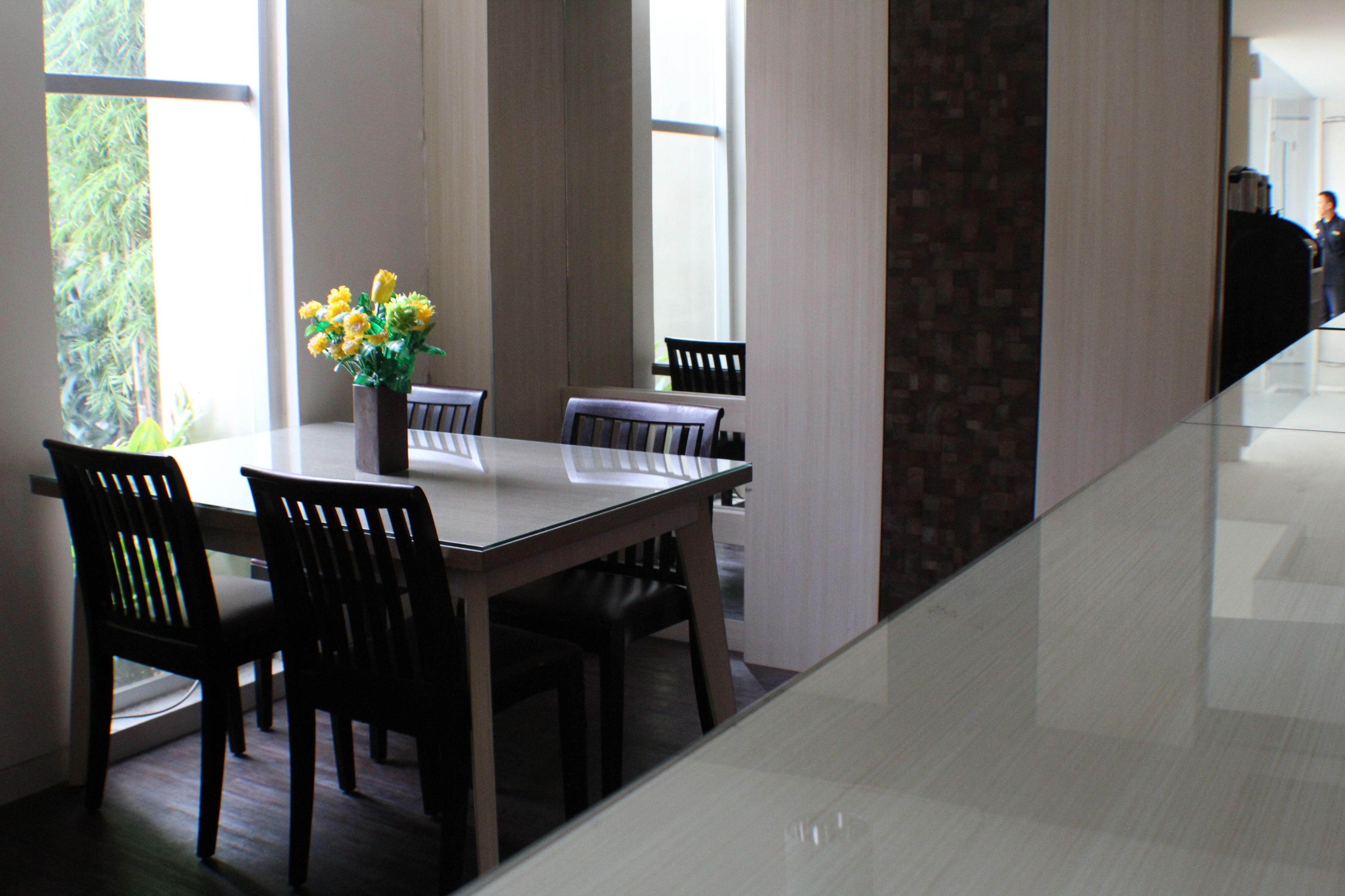 A modern dining area with a glass table, dark wooden chairs, and a vase of yellow flowers.