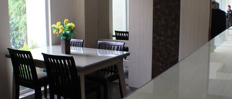 A modern dining area with a glass table, dark wooden chairs, and a vase of yellow flowers.