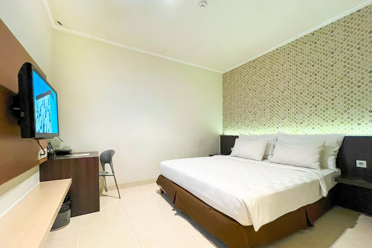 Una habitación de hotel con cama, escritorio, silla, televisor y pared con diseño.