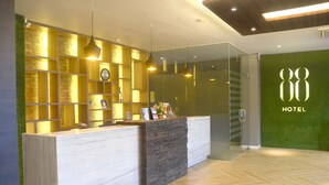 A hotel reception desk with a modern design, featuring a light-colored wood finish and a glass partition. - Hotel 88 Embong Kenongo by WH (Surabaya)
