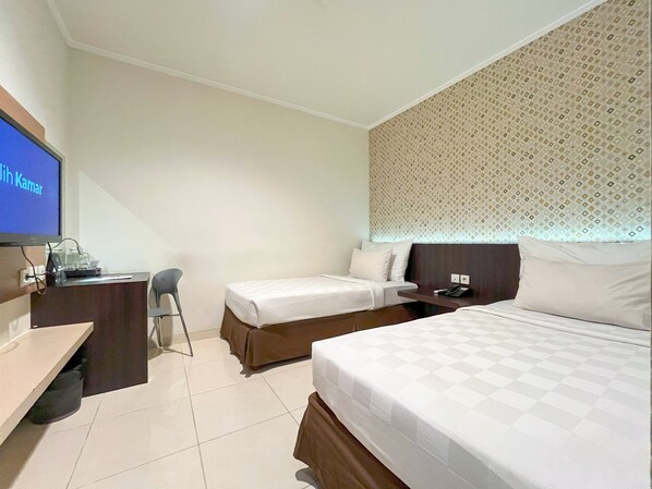 A hotel room with two beds, a desk, a chair, and a television.