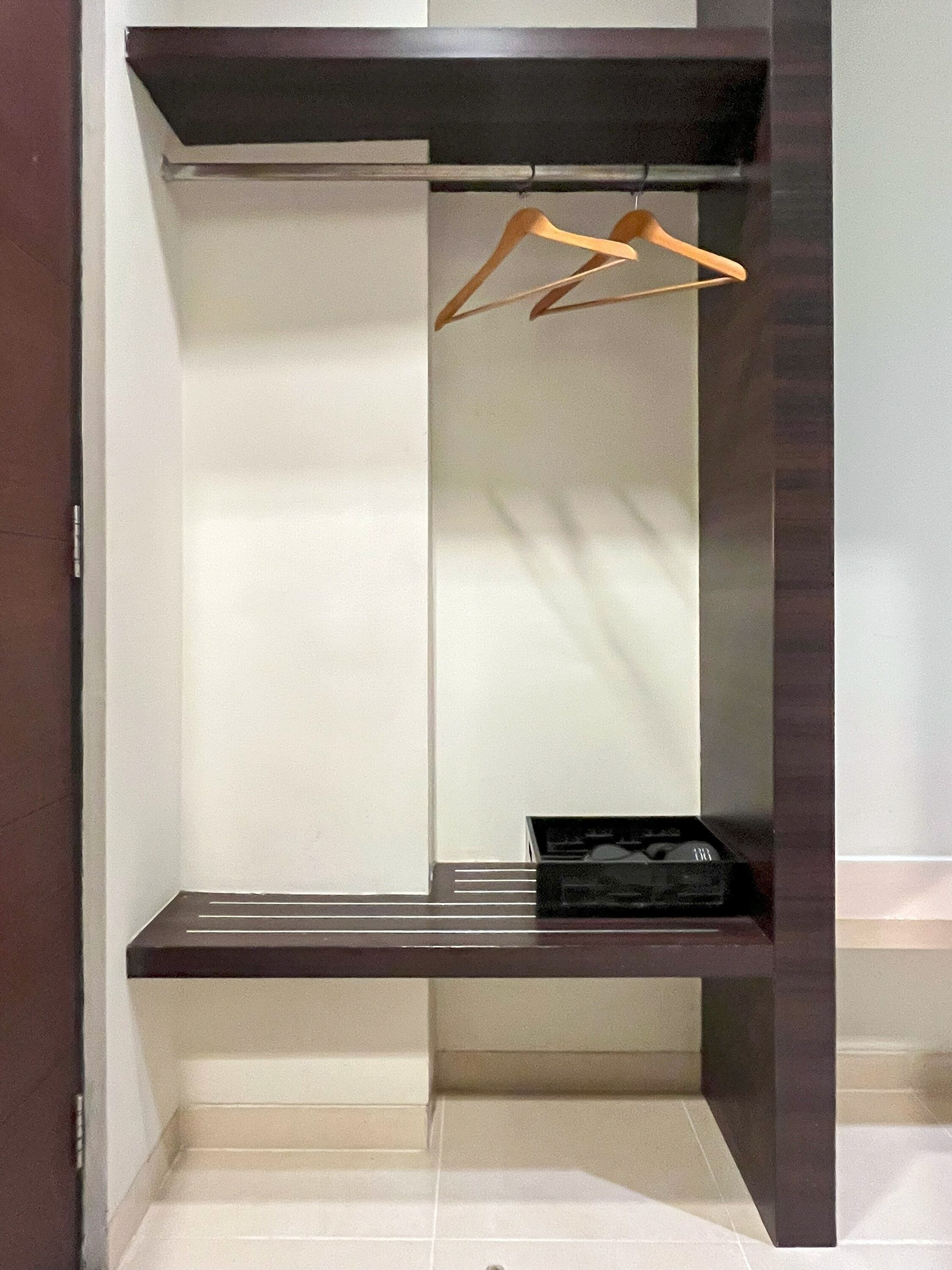 A walk-in closet with a dark wood finish, a hanging rod, and a bench with a black storage box.