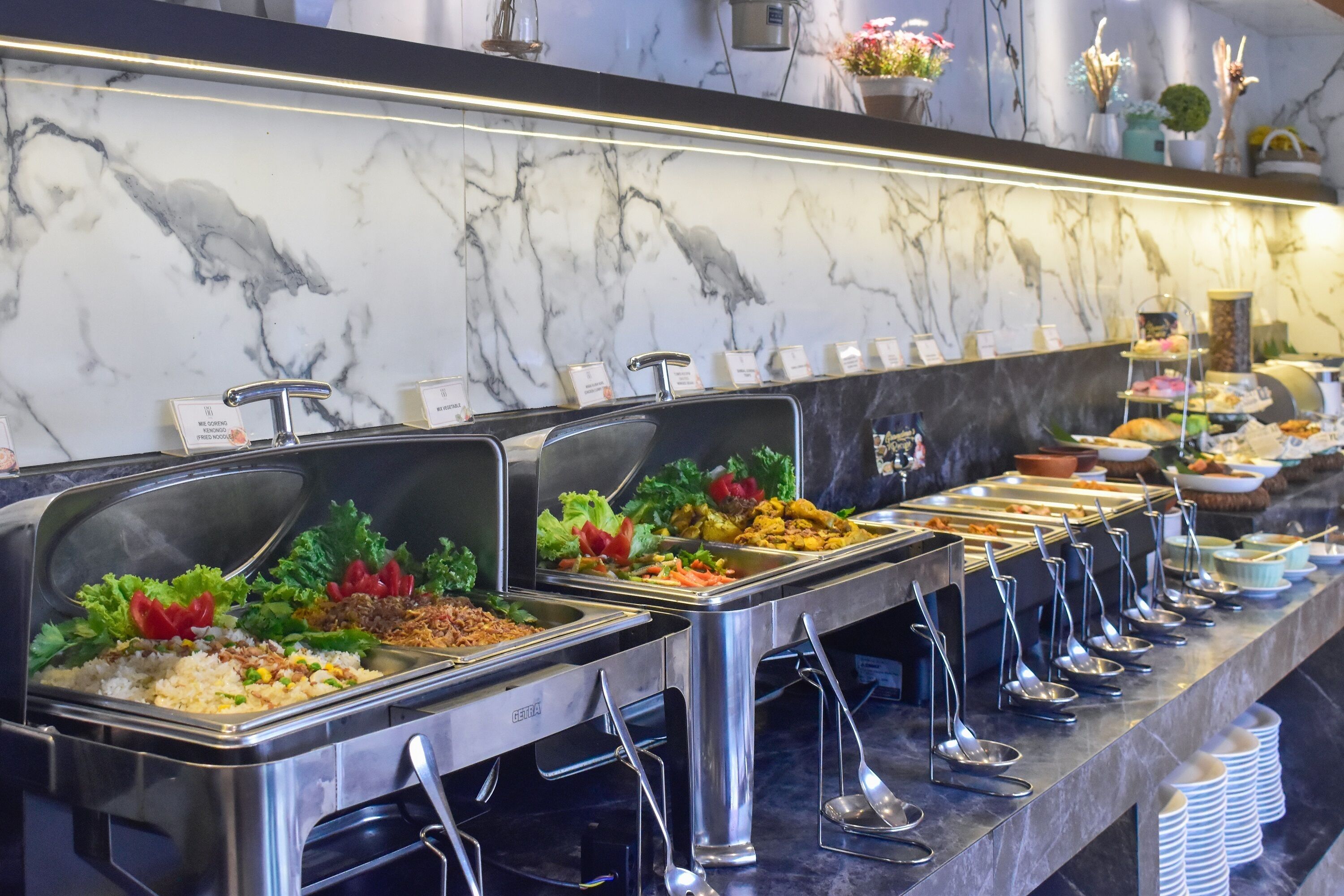A buffet with various food options, including salads, rice, and other dishes, arranged on a marble countertop with metal serving utensils.