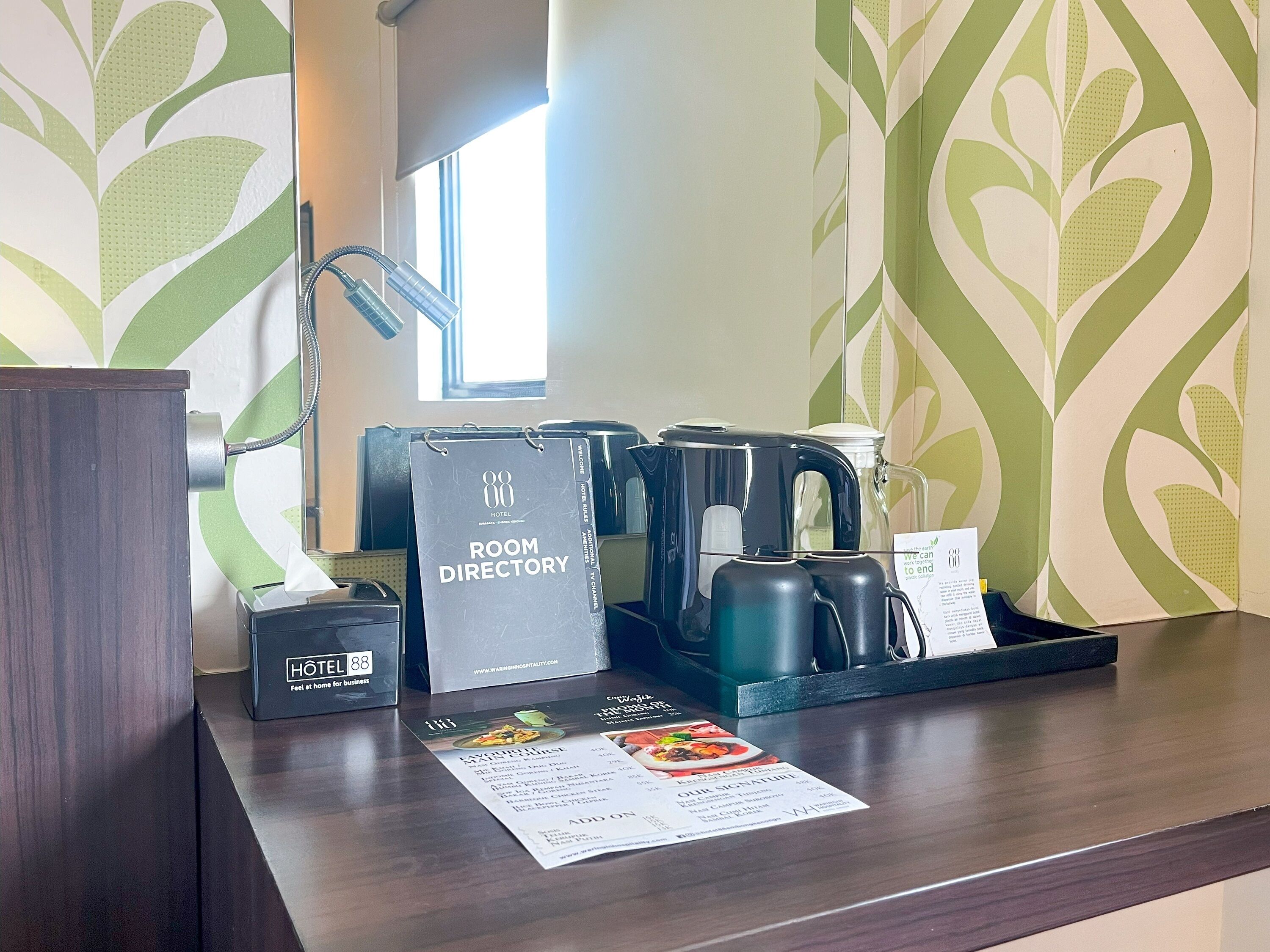 A hotel reception desk with a room directory, a coffee maker, a kettle, and a menu.