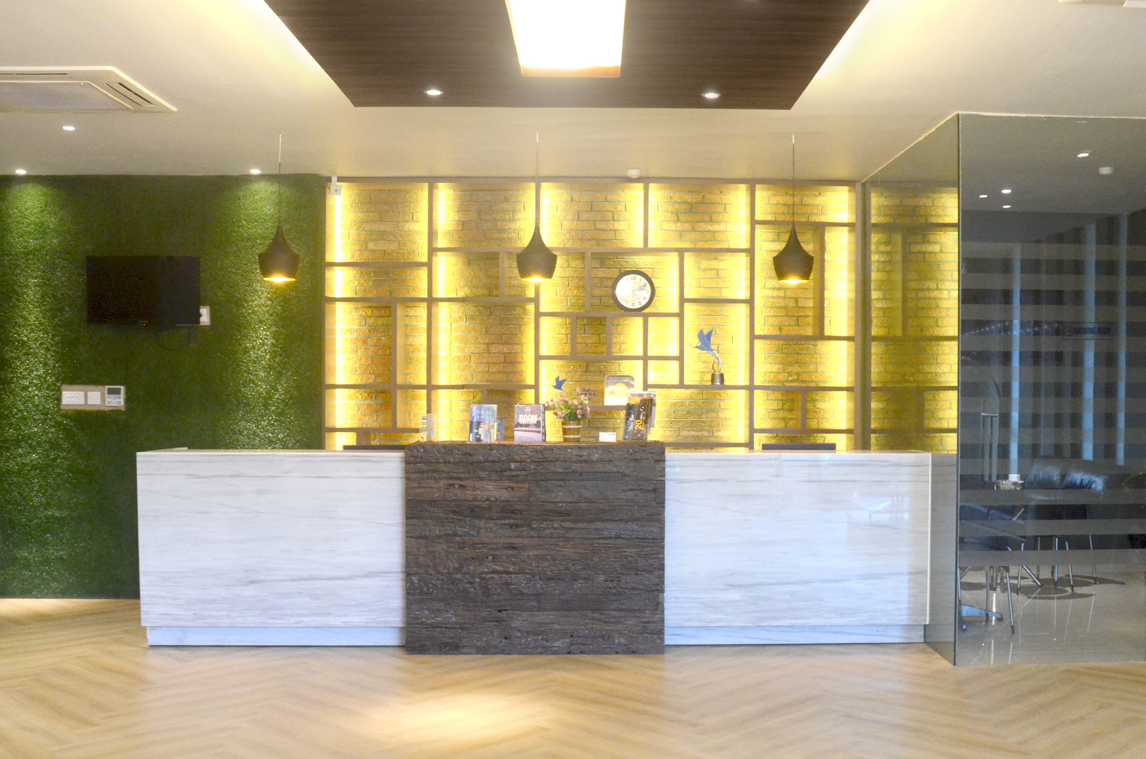 A reception desk with a green wall and a wooden accent in the center, a clock, and pendant lights.