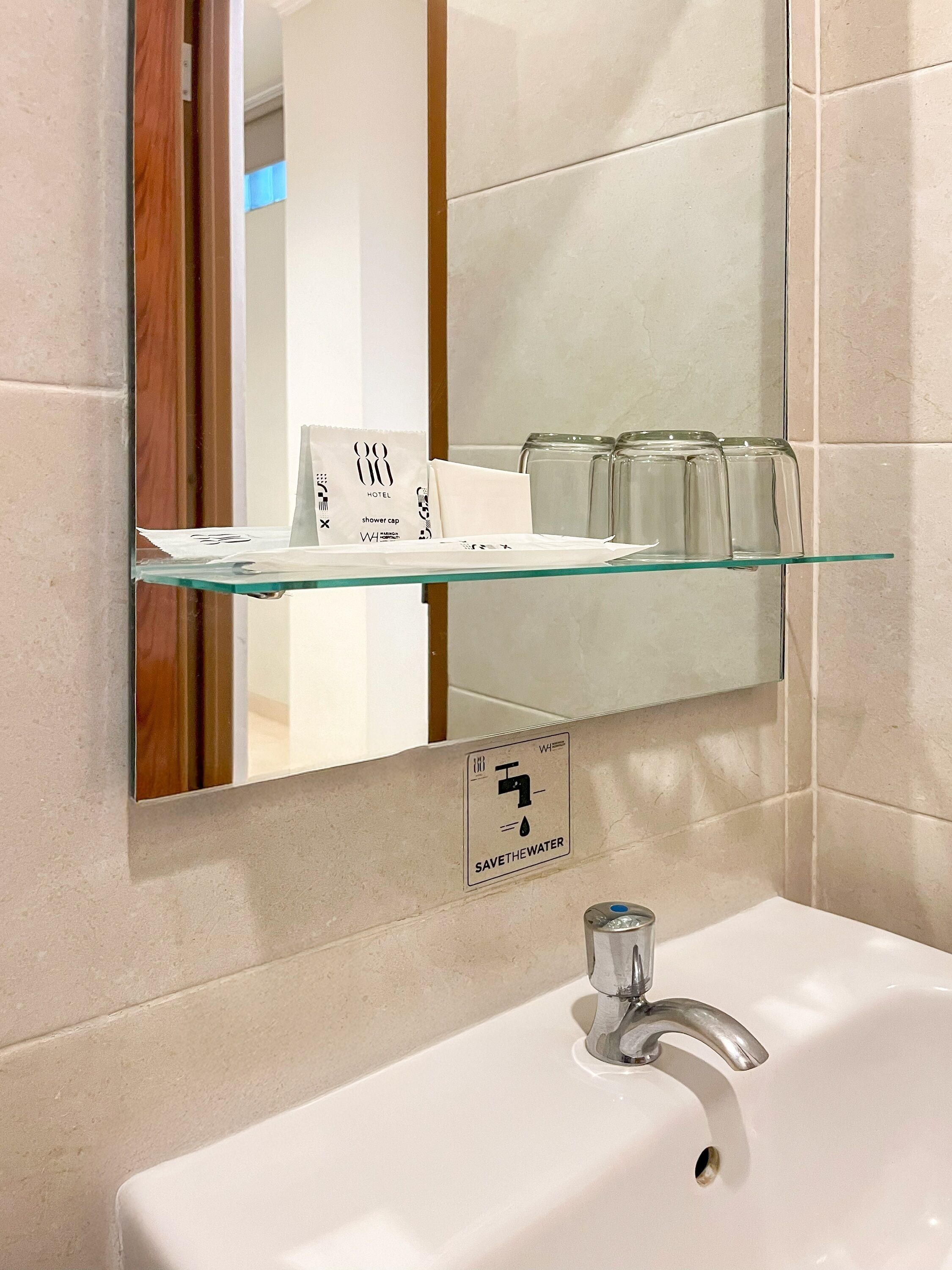 A bathroom with a glass shelf holding toiletries, a sink with a faucet, and a 'SAVETHEWater' sign.