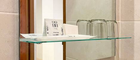 A bathroom with a glass shelf holding toiletries, a sink with a faucet, and a 'SAVETHEWater' sign.