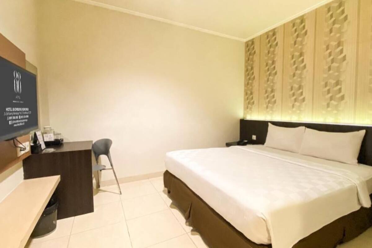 Habitación de hotel con cama, escritorio, silla, televisión y un panel decorativo en la pared.