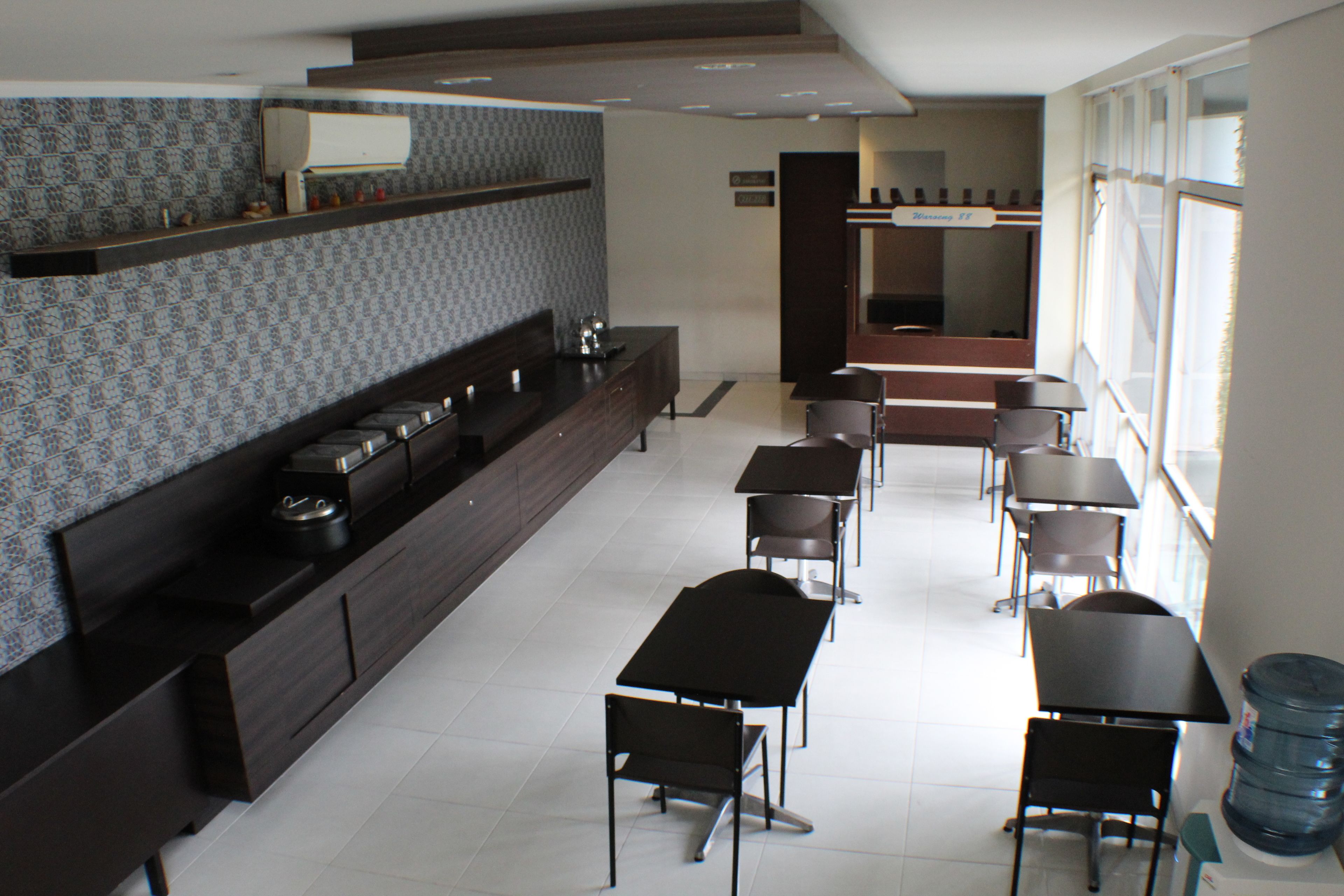 A modern hotel dining area with a long counter, multiple tables, and chairs.