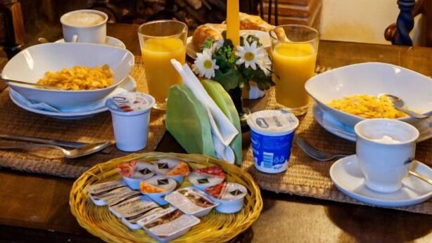 A breakfast table with plates of food, cups, a candle, and a fireplace in the background. - Hotel Melecchi (Lucca)