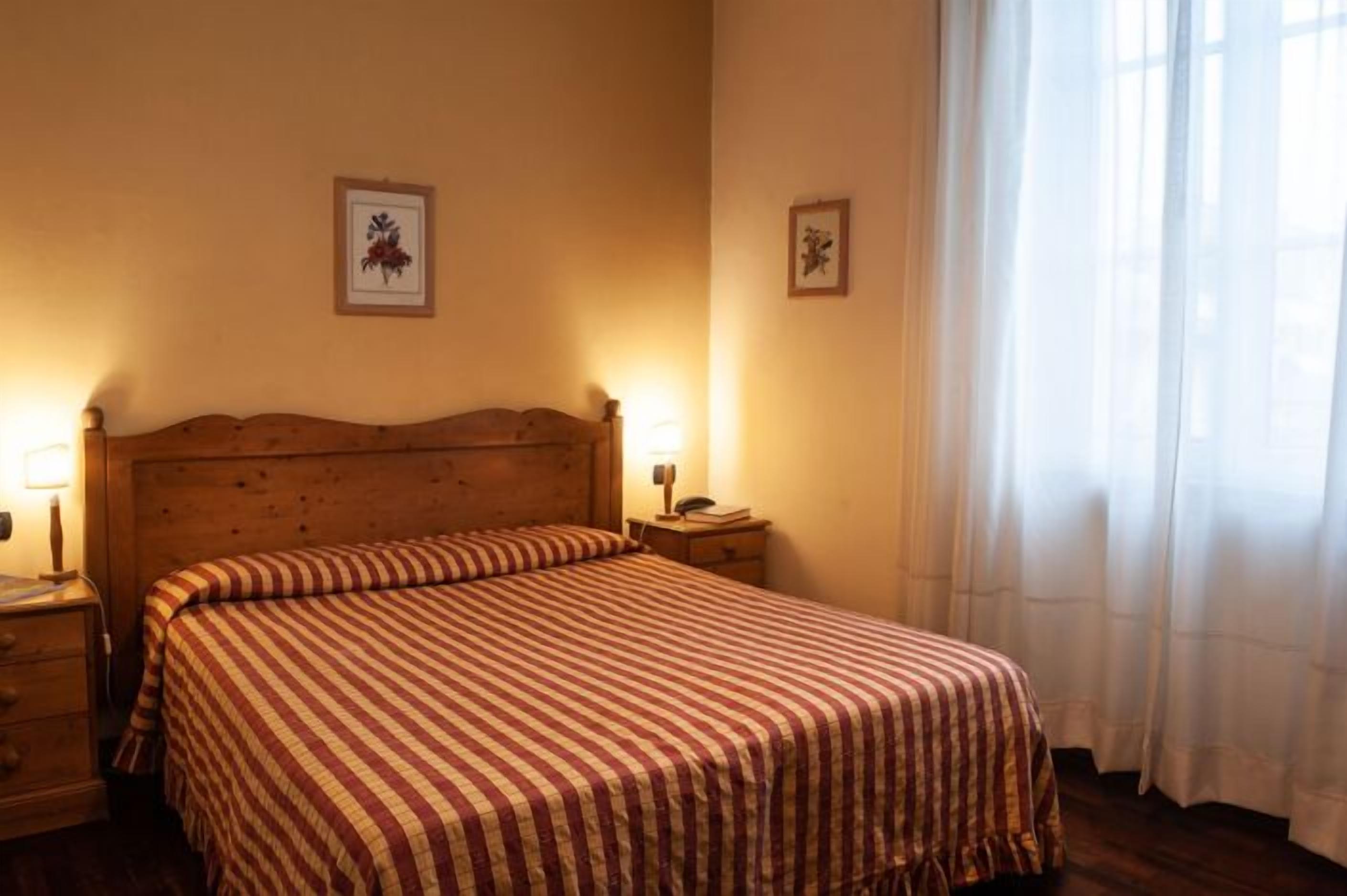 A bedroom with a wooden headboard, a striped bedspread, two bedside lamps, and framed artwork on the walls.