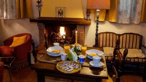 A cozy room with a fireplace, a dining table set with breakfast, and comfortable seating. - Hotel Melecchi (Lucca)
