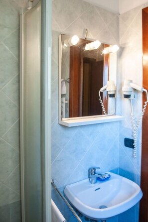 Une salle de bain avec une douche à parois de verre, un lavabo avec un miroir au-dessus et deux sèche-cheveux fixés au mur.