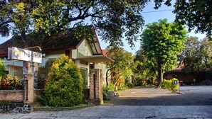 A hotel entrance with a sign, a paved driveway, and surrounding greenery.