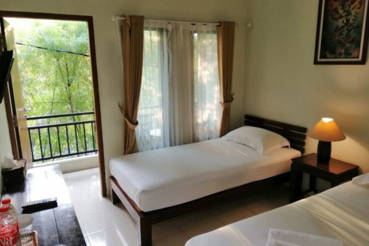 Una cama individual con estructura de madera, una mesita de noche con lámpara y una ventana con cortinas.