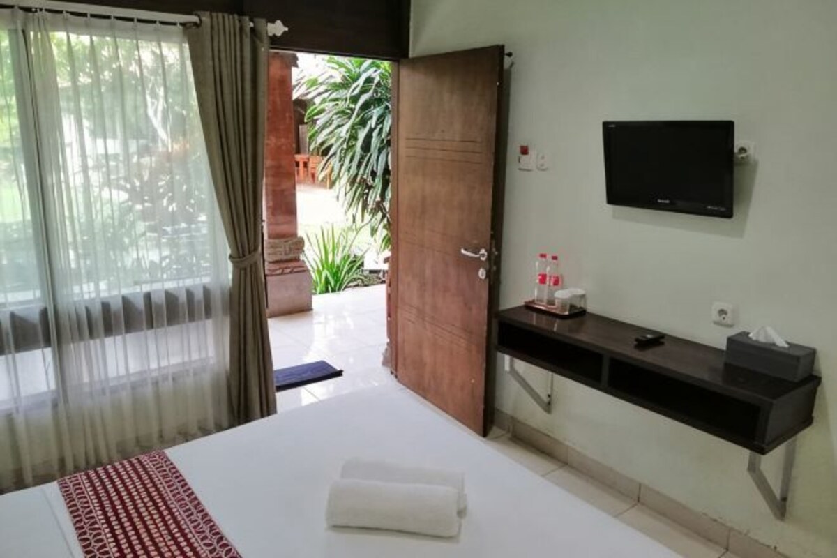 A hotel room with a bed, a TV, a bedside table, and a door leading to a balcony.