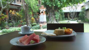 A table with plates of food and a cup, set against a backdrop of a garden with trees and a building.