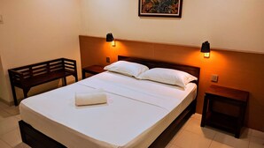 A hotel room with a single bed, two bedside tables, a bench, and a wall-mounted light fixture.