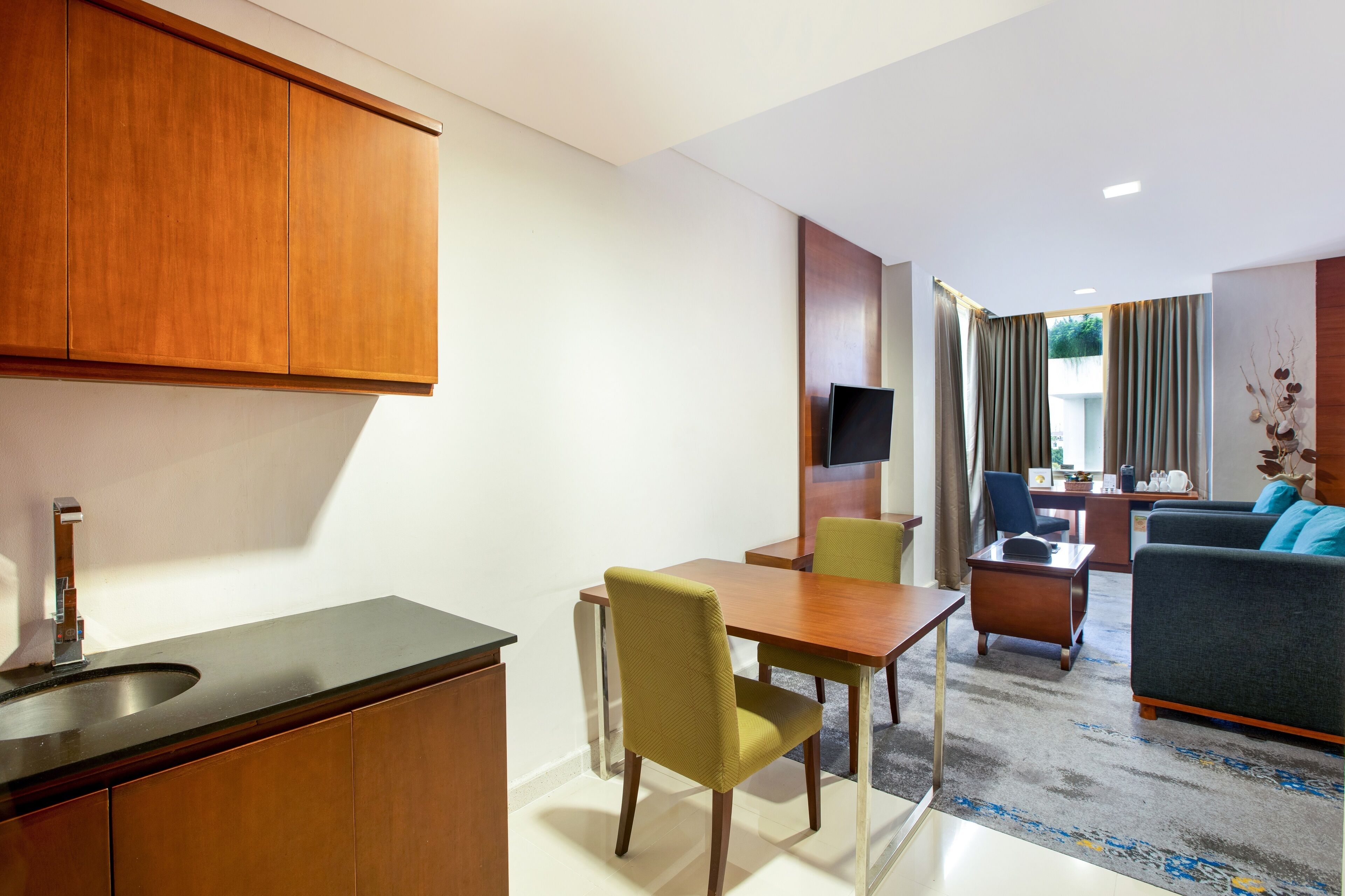 A modern hotel room with a kitchenette, dining area, and living space.