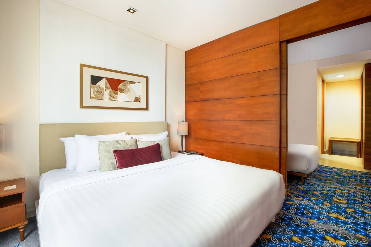Une chambre d’hôtel avec un grand lit, un mur recouvert de panneaux en bois, un tableau encadré et une moquette à motifs.