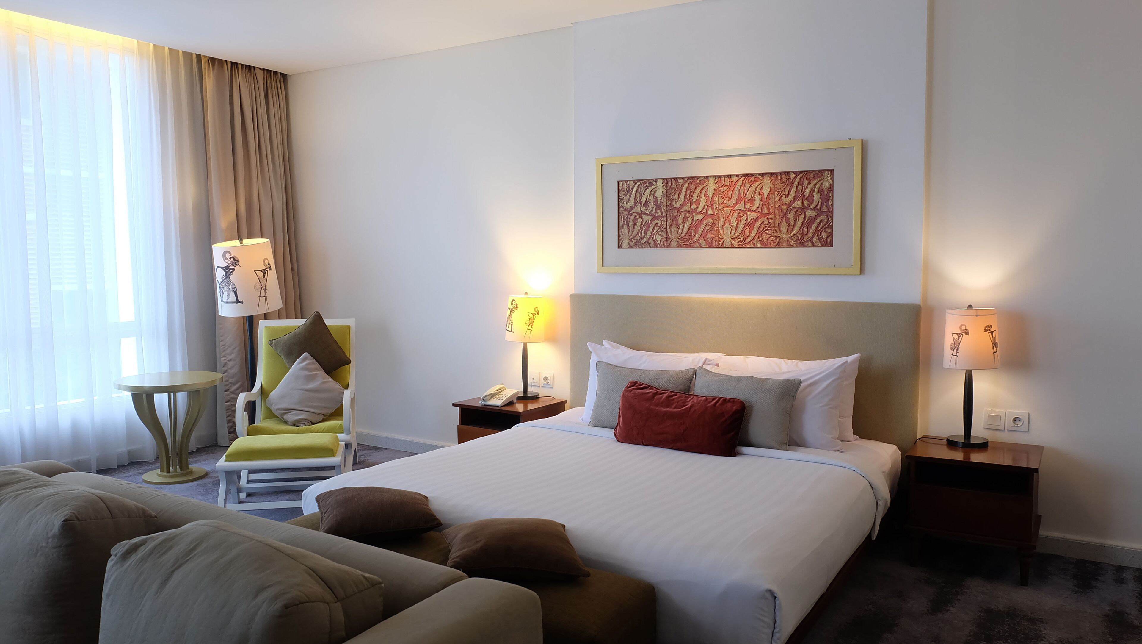 Een hotelkamer met een bed, twee nachtkastjes, een stoel, een klein tafeltje en een bank.