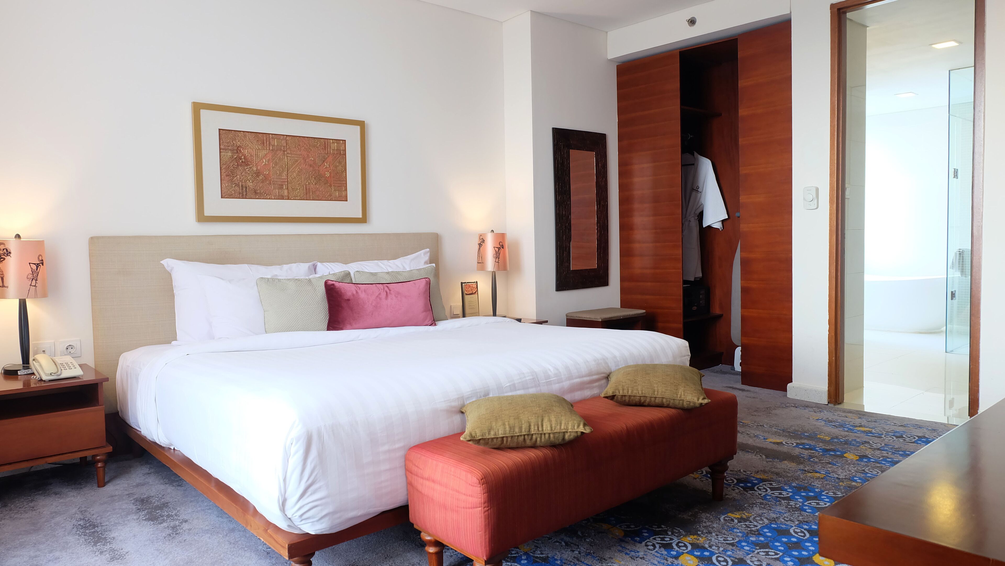 A hotel room with a large bed, bedside lamps, a wooden wardrobe, and a patterned carpet.