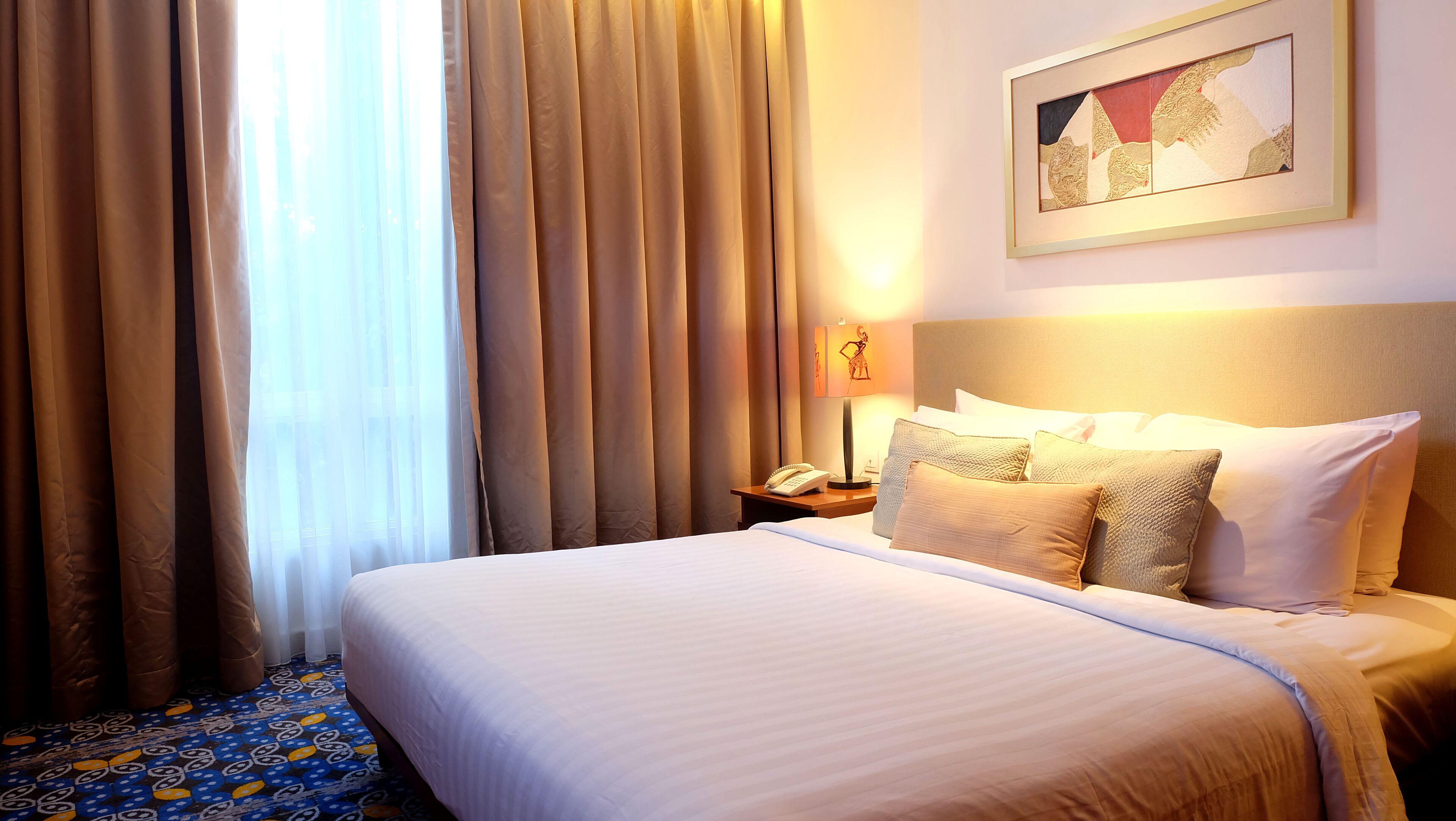 A hotel room with a large bed, a nightstand with a lamp, and a painting on the wall.